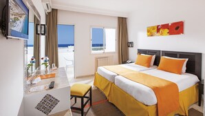 A hotel room with a bed, a desk with a computer, a chair, and a window with a view of the sea.