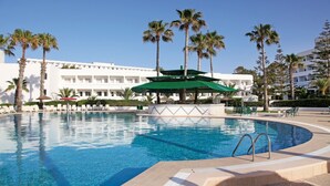 A swimming pool with a green umbrella, palm trees, and a white building in the background.