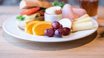 A plate of food including cheese, grapes, and a sandwich, with a glass of orange juice and a glass of tea in the background.