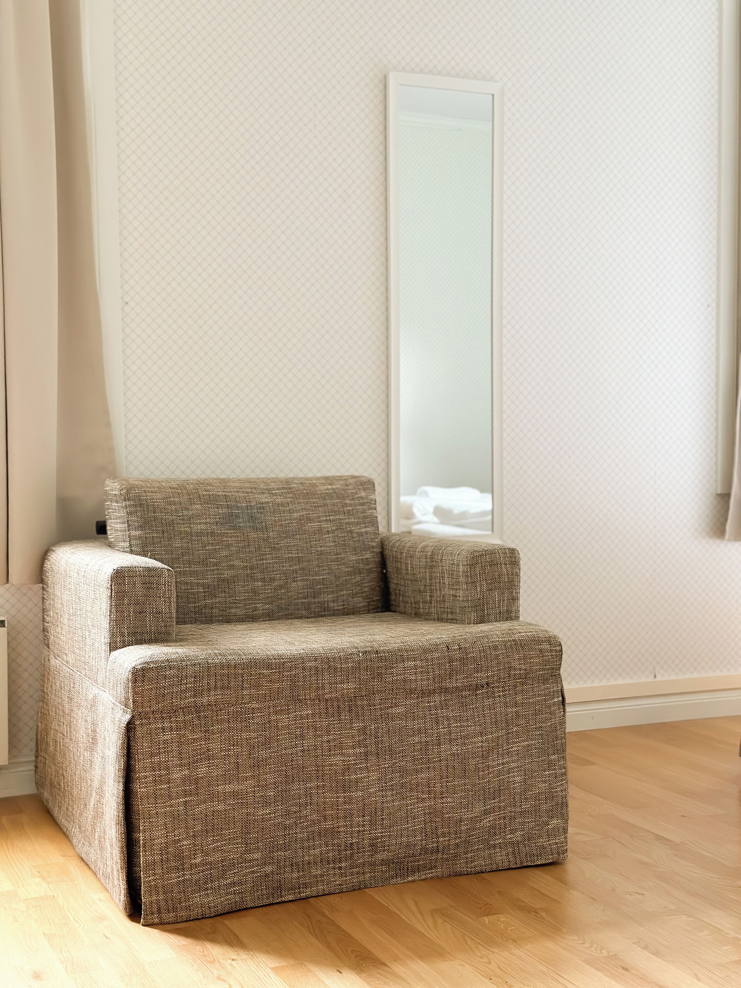 Ein Zimmer mit einem braunen gewebten Sofa, einem großen Spiegel und einem Holzboden.