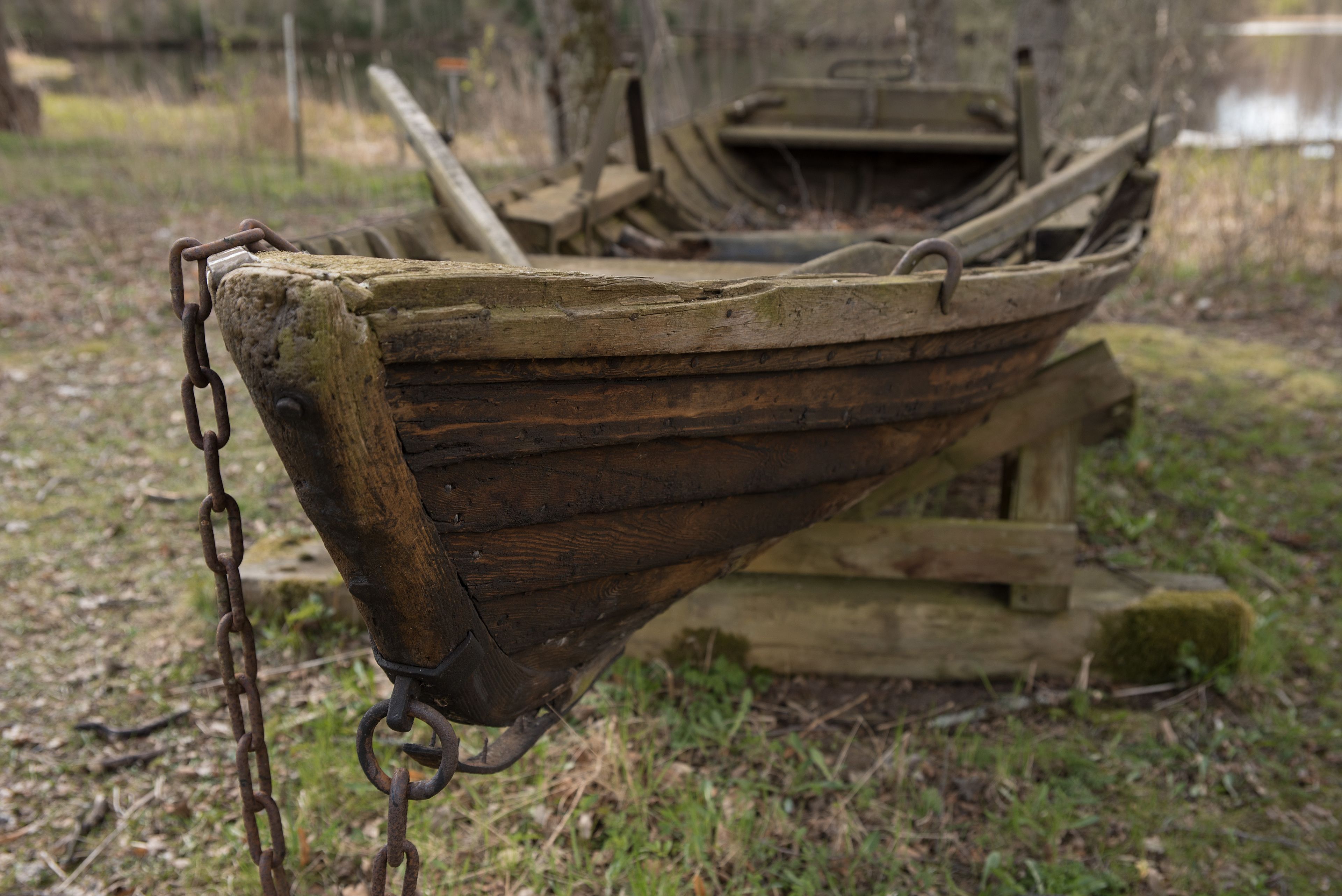 A wooden boat with a chain attached to its front, resting on a grassy area.