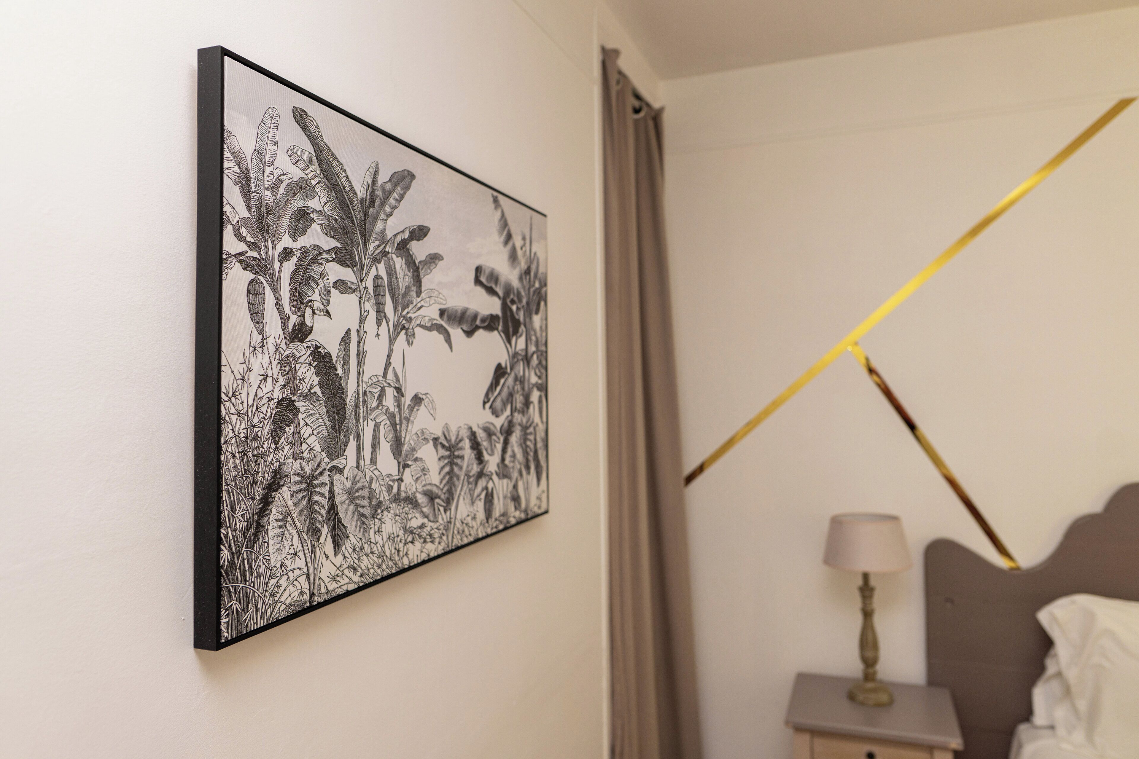 Et soveværelse med en seng, et natbord med en lampe, og et vægmaleri med tropiske planter.