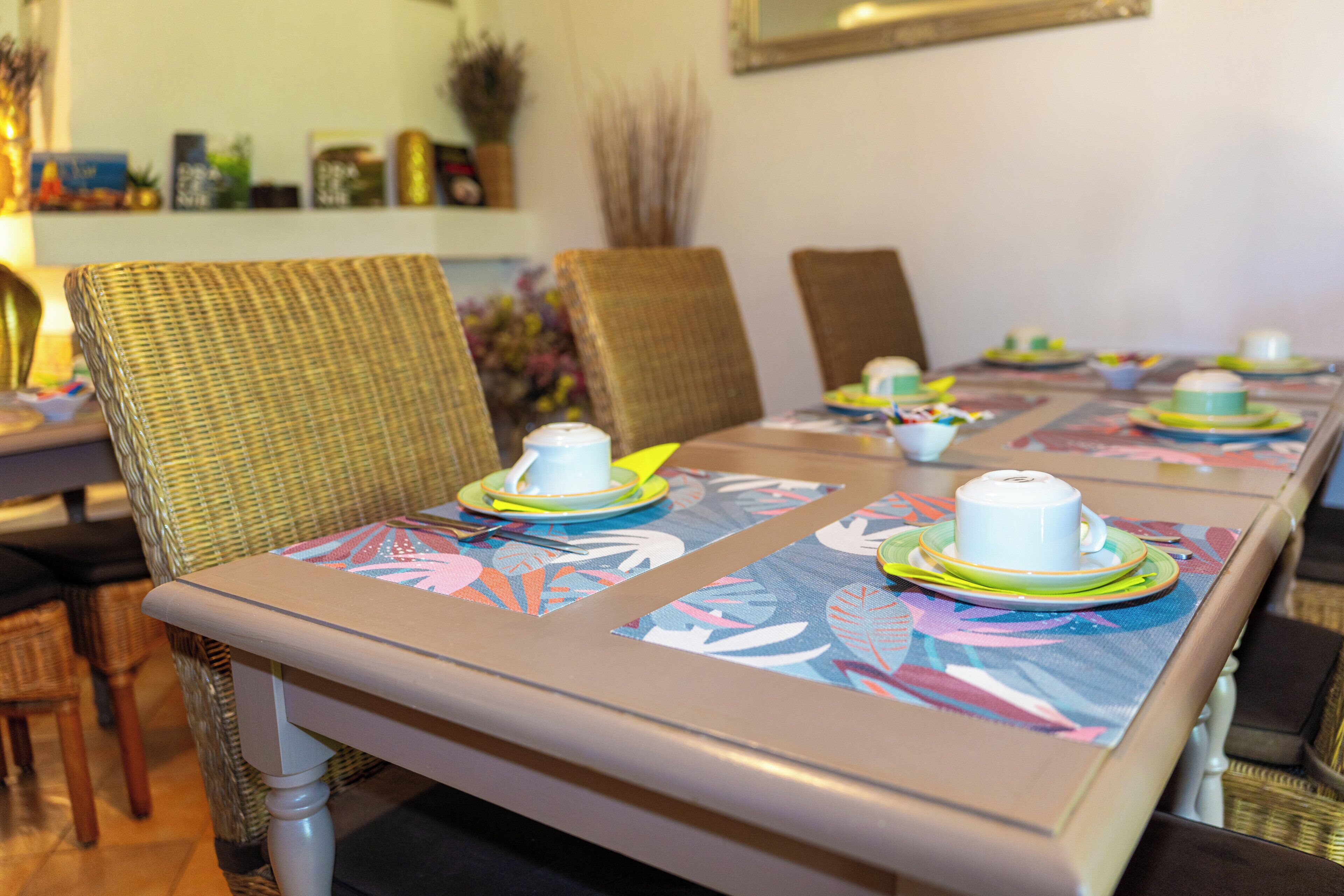 Una mesa de comedor con manteles florales, platos blancos y una taza blanca.