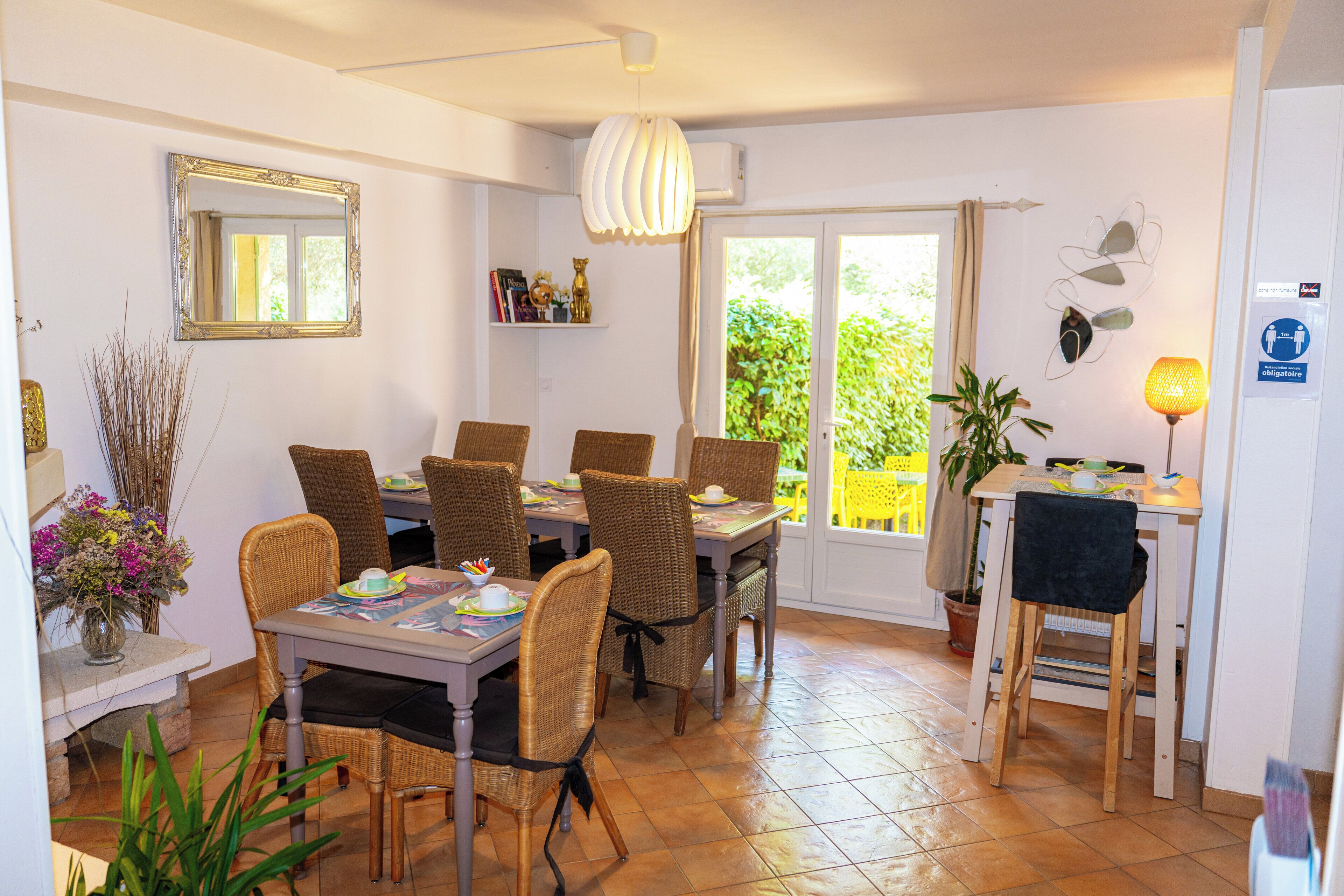 Un comedor con sillas de mimbre, una mesa con mantel individual, un espejo y una planta en maceta.