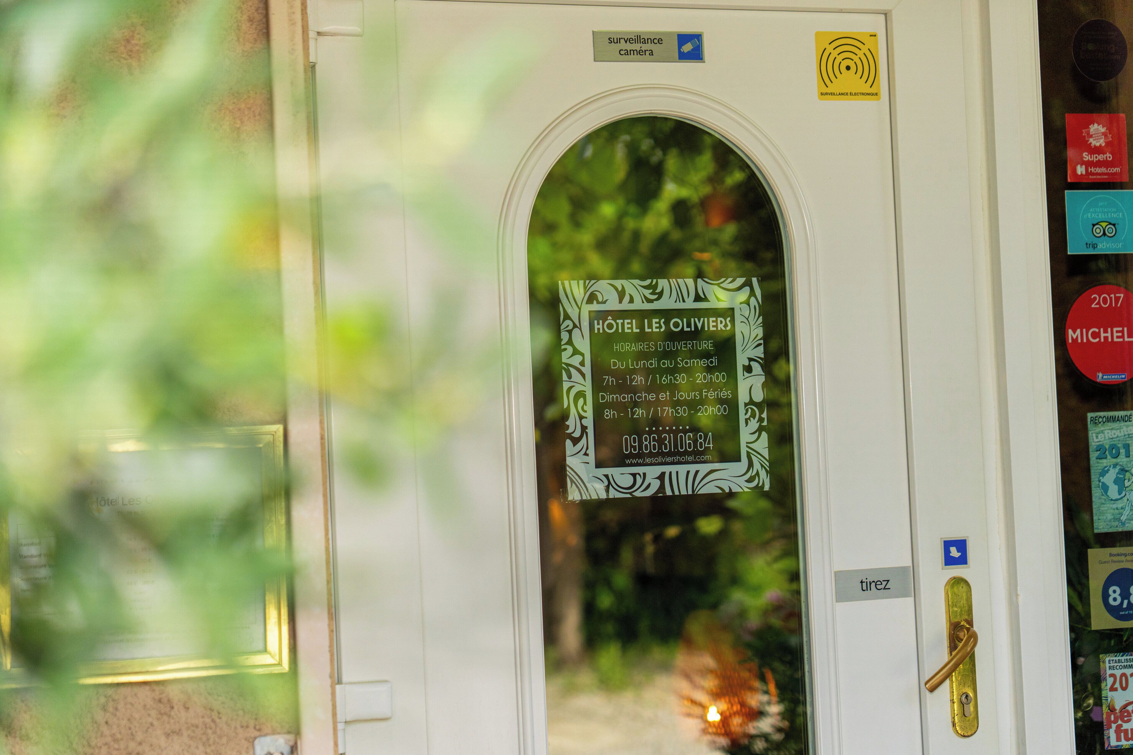 Puerta de hotel con un cartel que indica los horarios de apertura y el símbolo de una cámara de seguridad.