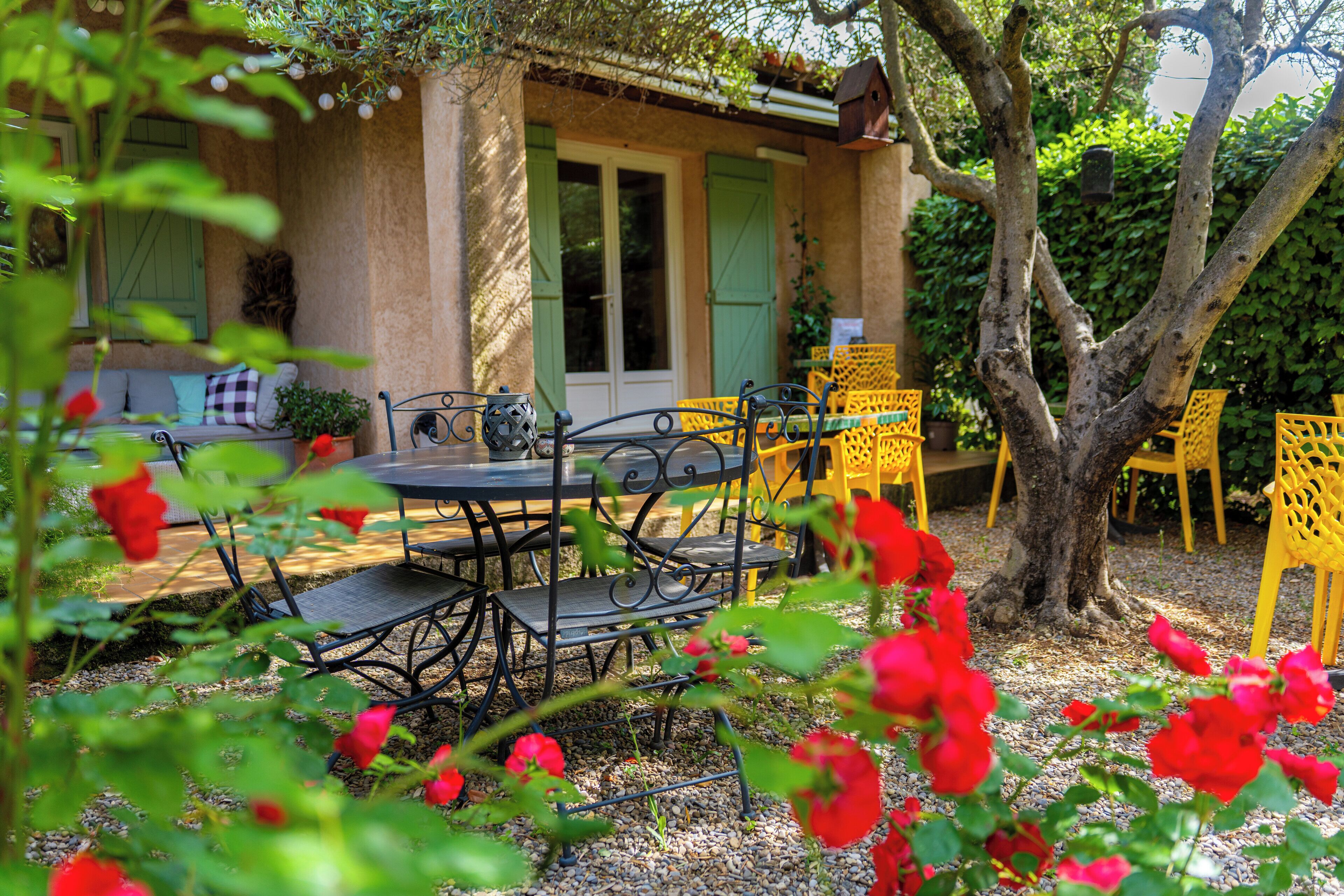 A patio with a table and chairs, surrounded by greenery and flowers.