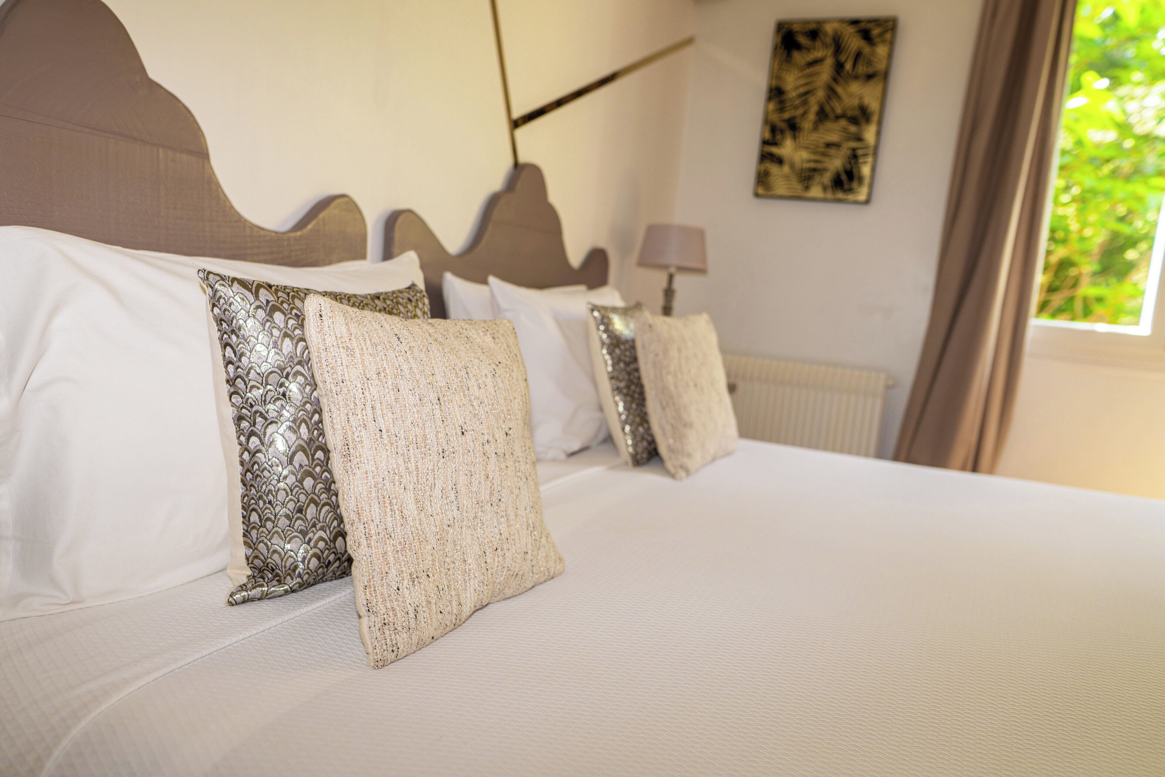 A neatly made bed with patterned and plain pillows, a headboard, and a window with curtains.