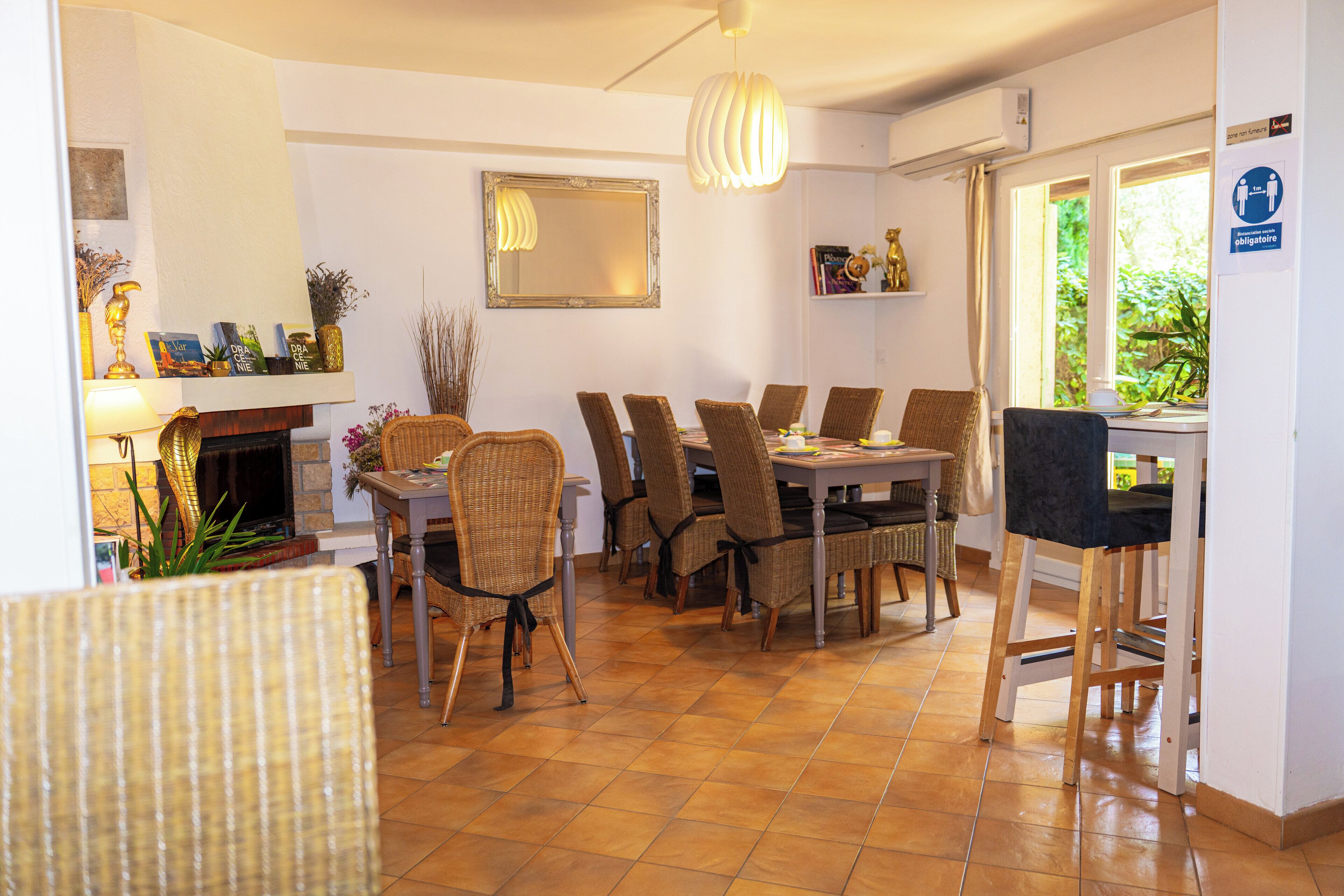 A dining area with a fireplace, wicker chairs, a wooden table, and a hanging light fixture.