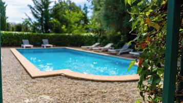 Una piscina con borde de guijarros, rodeada de sillones de descanso y vegetación.