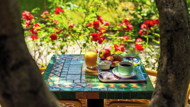 Una mesa con alimentos para el desayuno, incluyendo un vaso de jugo de naranja, una manzana, croissants y una taza de café.