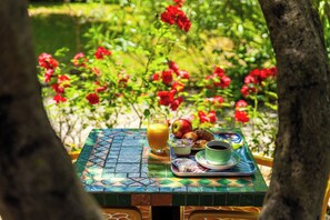Una mesa con alimentos para el desayuno, incluyendo un vaso de jugo de naranja, una manzana, croissants y una taza de café.