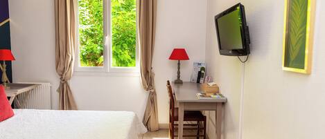 Un dormitorio con cama, escritorio, silla, televisor y ventana con cortinas.