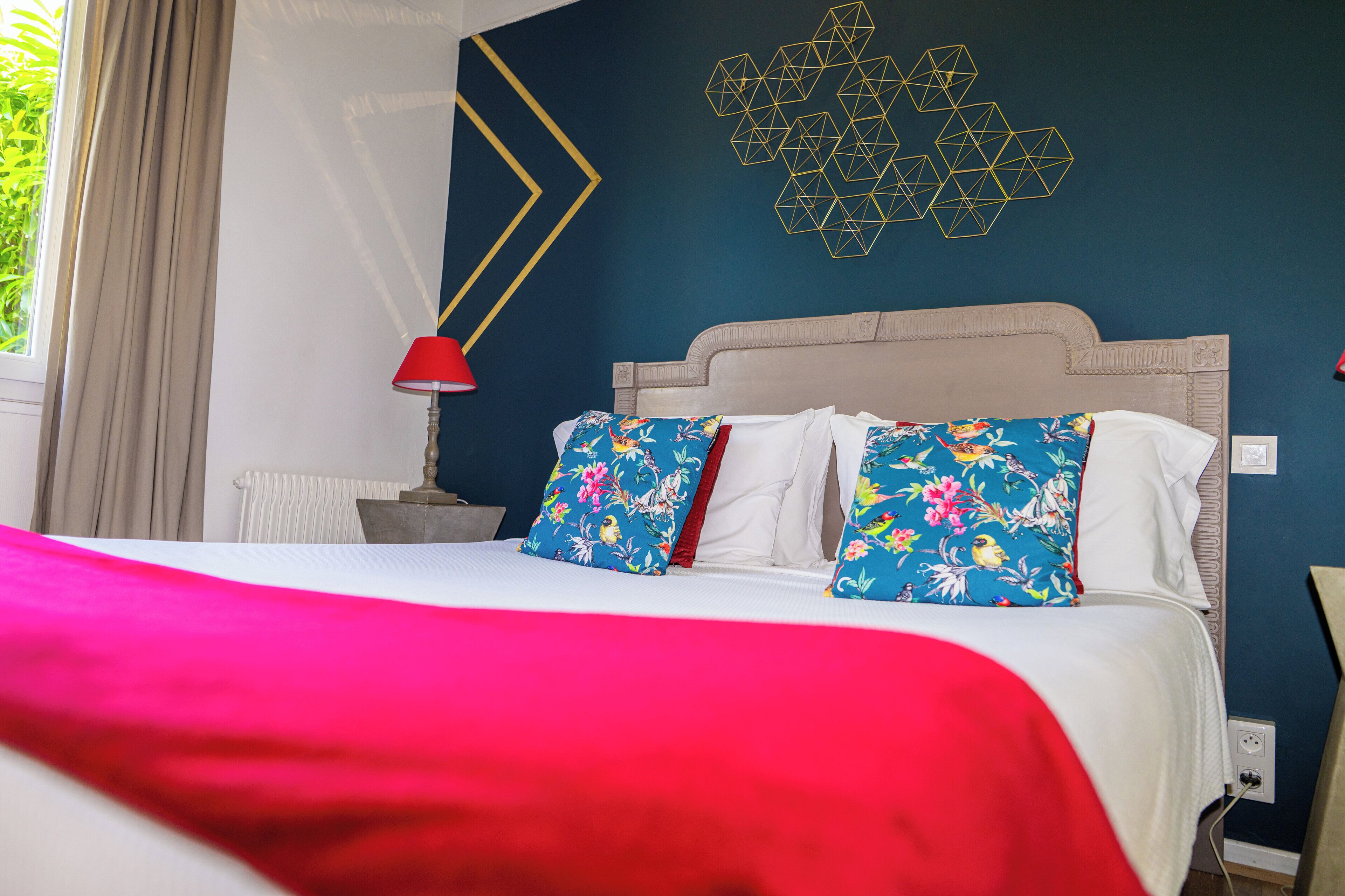 Hotellihuone, jossa on sänky, yöpöytä, lamppu ja geometrisesti kuvioitu seinäkoriste.
