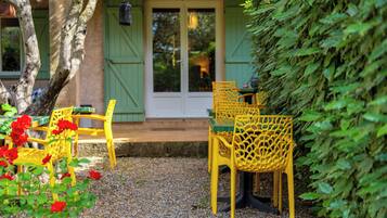 An outdoor seating area with yellow chairs and a table, surrounded by greenery and a gravel path.