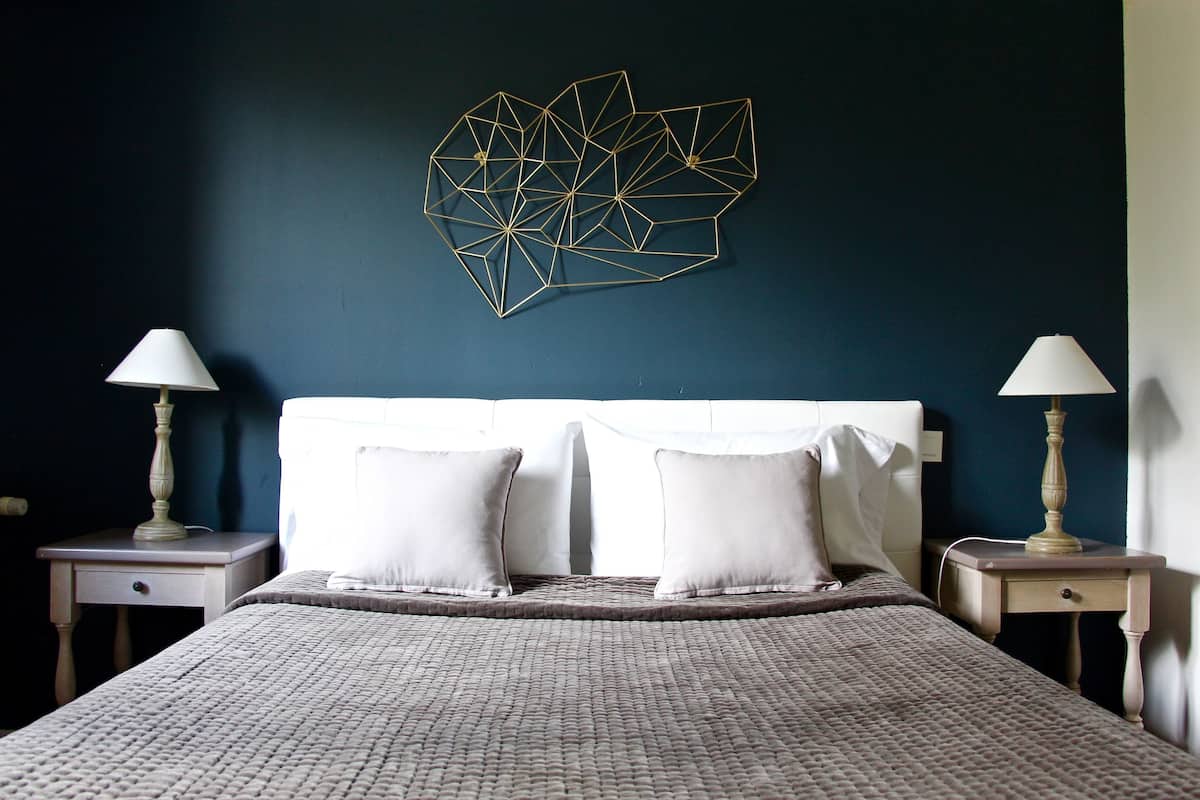 Una cama bien tendida con un edredón texturizado, dos mesitas de noche con lámparas y un adorno geométrico en la pared.