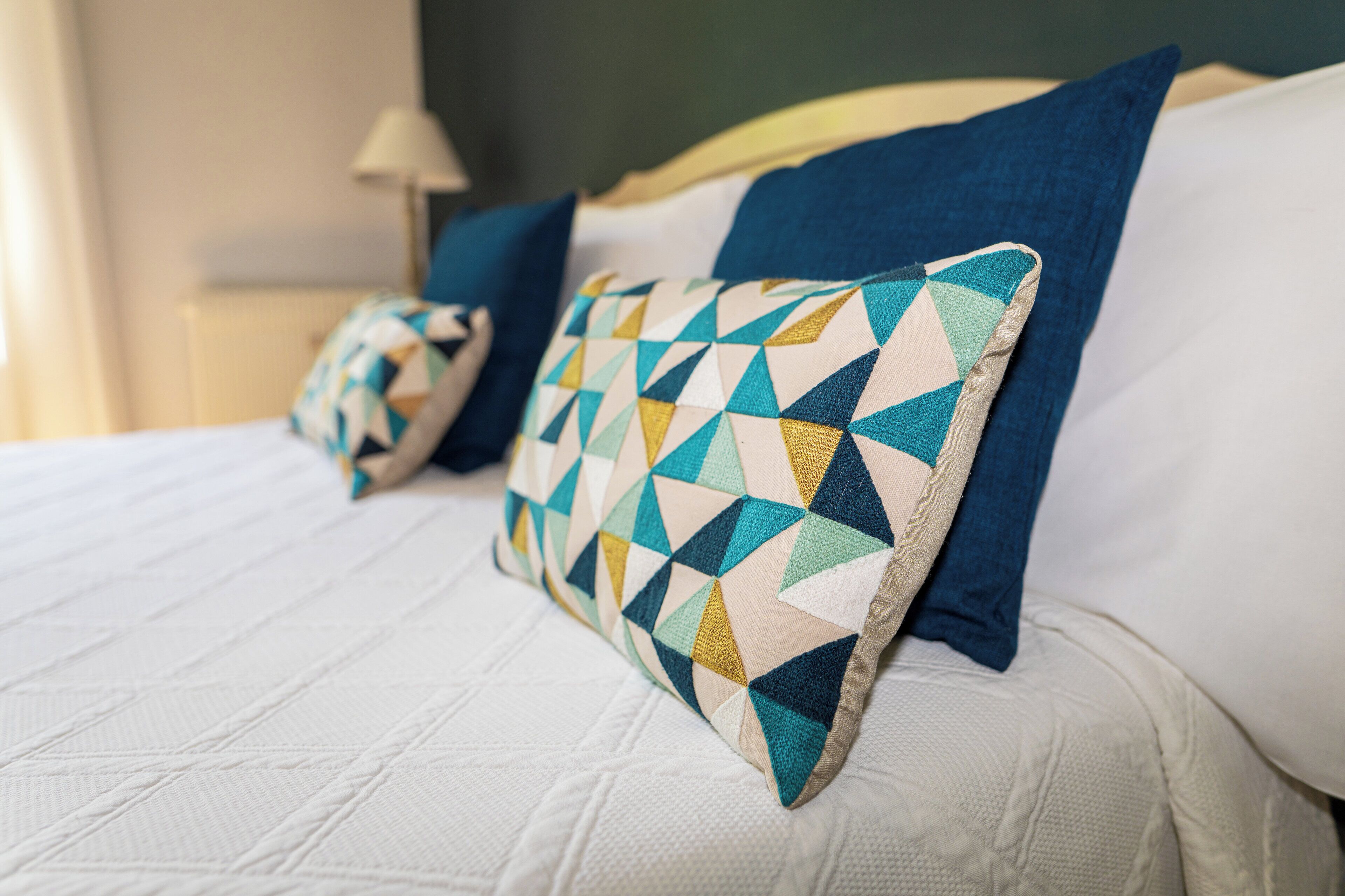 Un lit recouvert d’une couette blanche matelassée, un oreiller bleu et un autre oreiller à motifs.