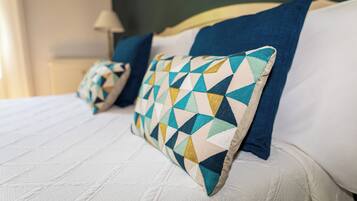 Un lit recouvert d’une couette blanche matelassée, un oreiller bleu et un autre oreiller à motifs.