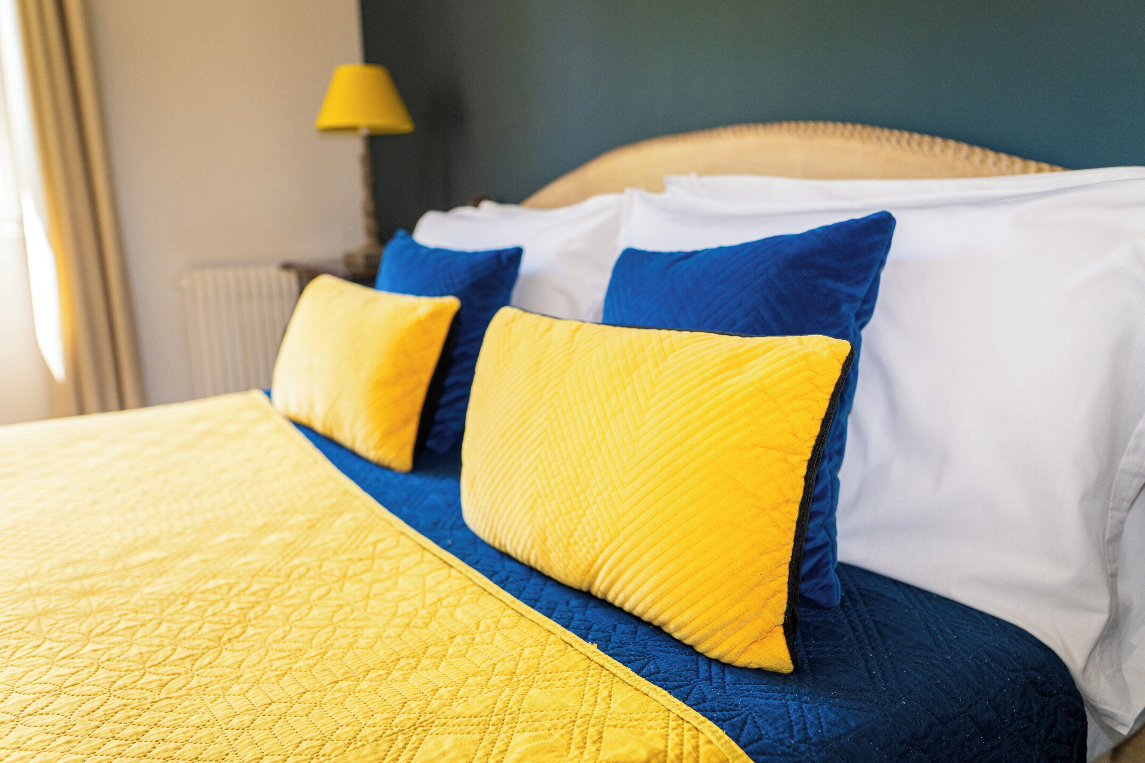 Una cama con colcha amarilla y almohadas azules y blancas.