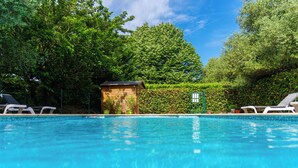 Una piscina con sillas de descanso, rodeada de vegetación y una pequeña construcción de madera.