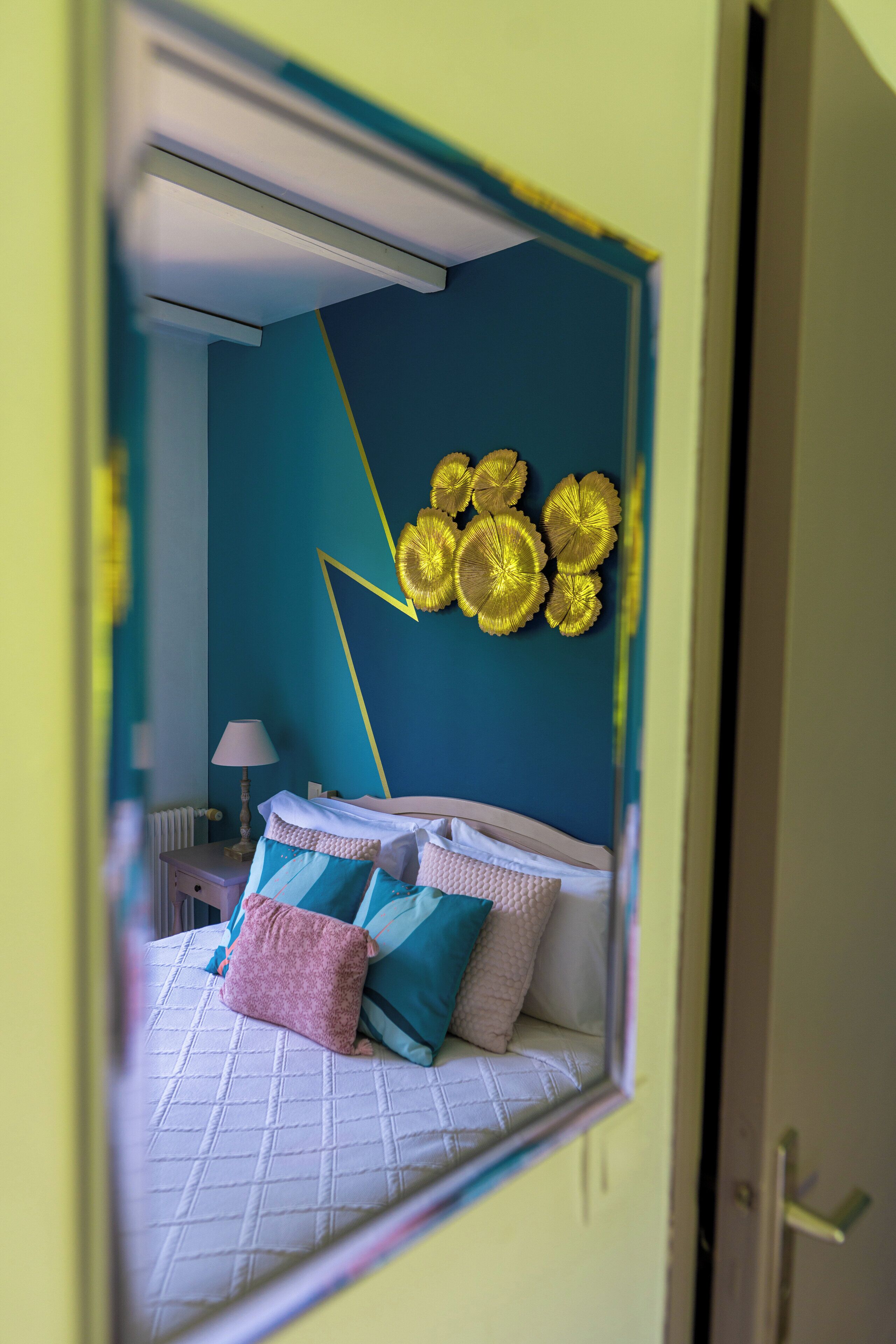Un dormitorio con cama, almohadas, una lámpara y una decoración en la pared.
