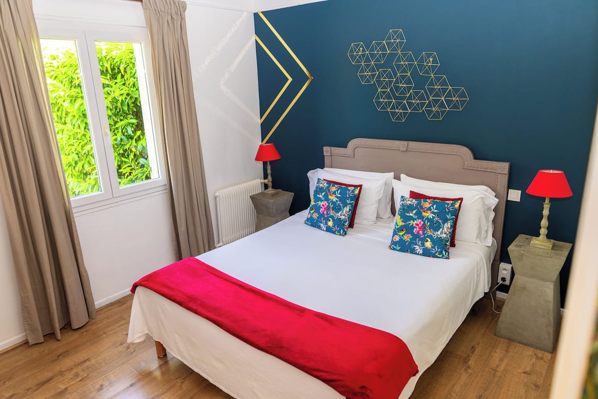 Un dormitorio con una cama, dos mesitas de noche, un ventanal con cortinas y un adorno geométrico en la pared.