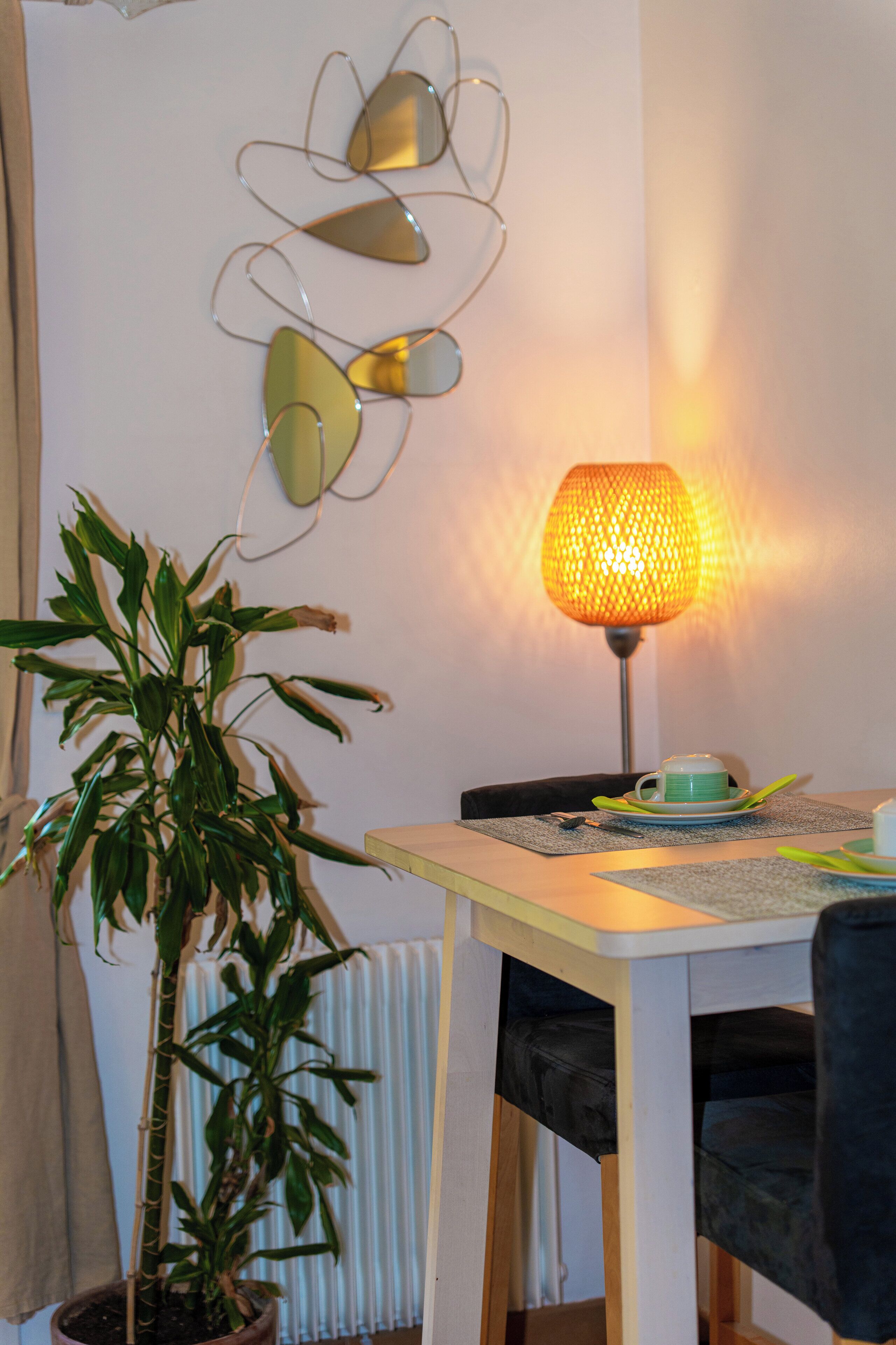 Un coin repas comprenant une table, des chaises, une plante en pot, une lampe et un élément décoratif fixé au mur.