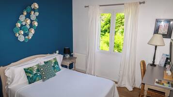 Un dormitorio con cama, mesita de noche, ventana con cortinas, una silla y una lámpara.