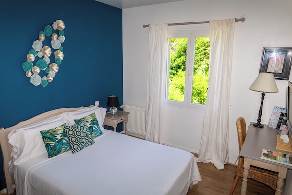 Un dormitorio con cama, mesita de noche, ventana con cortinas, una silla y una lámpara.