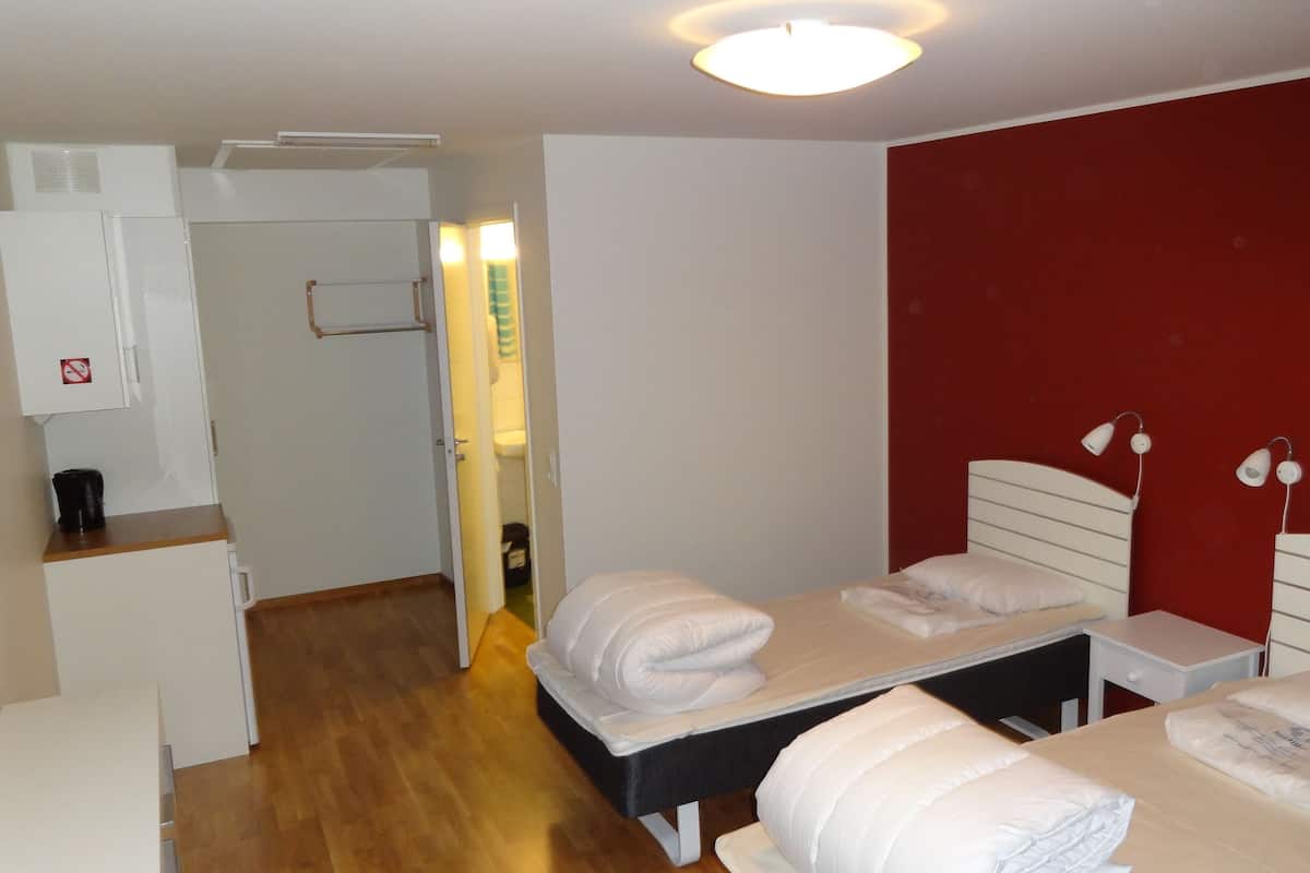 A hotel room with two beds, a small desk, a coffee machine, and a red accent wall.