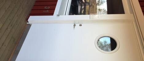 A white door with a circular window and a small doorbell.