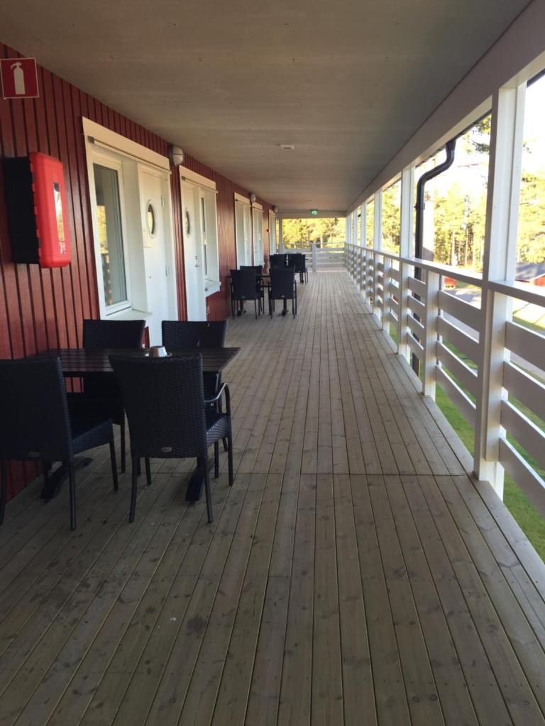 A covered outdoor area with tables and chairs, a wooden floor, and a railing.