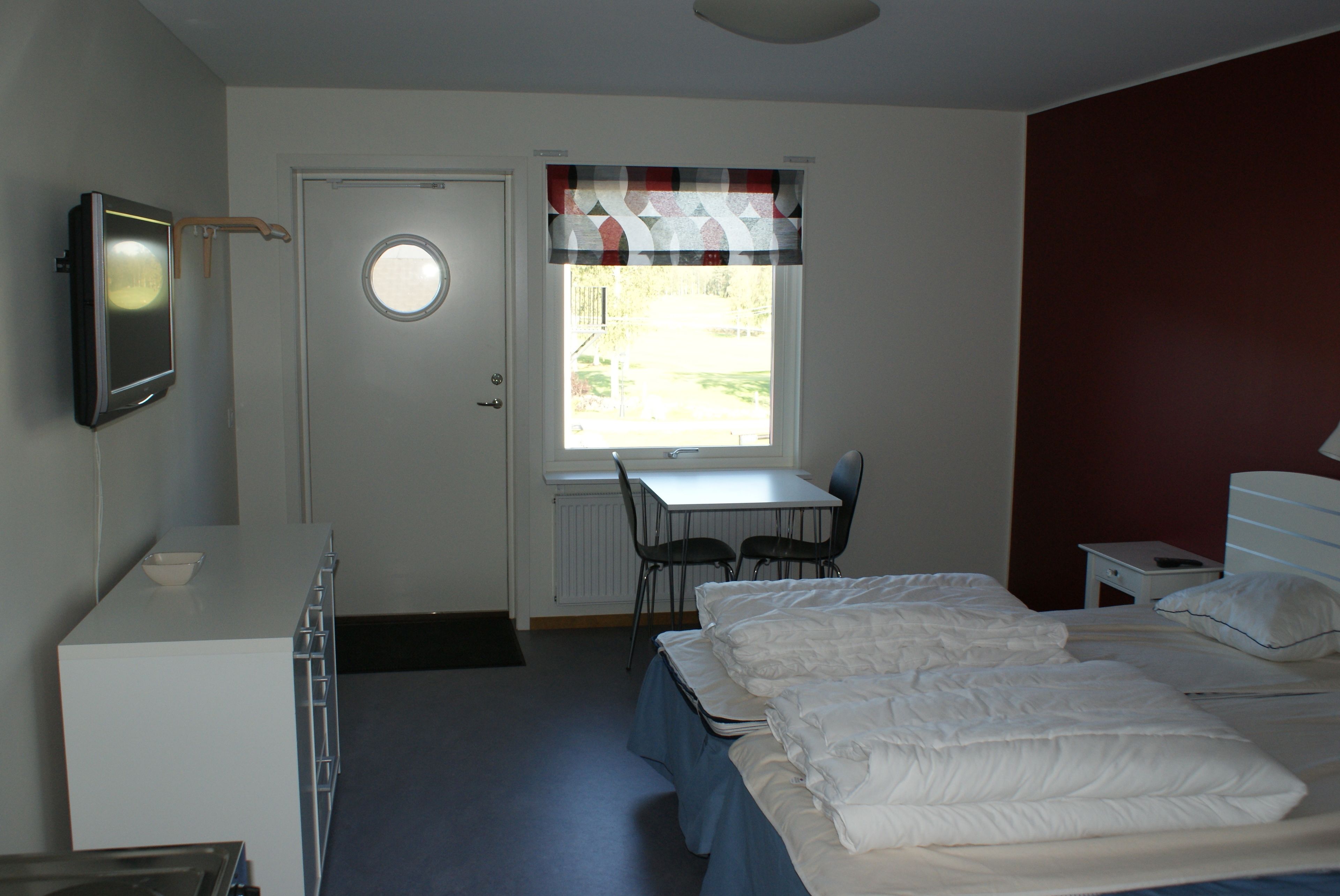 A hotel room with a bed, a desk, a chair, a TV, and a window with a curtain.