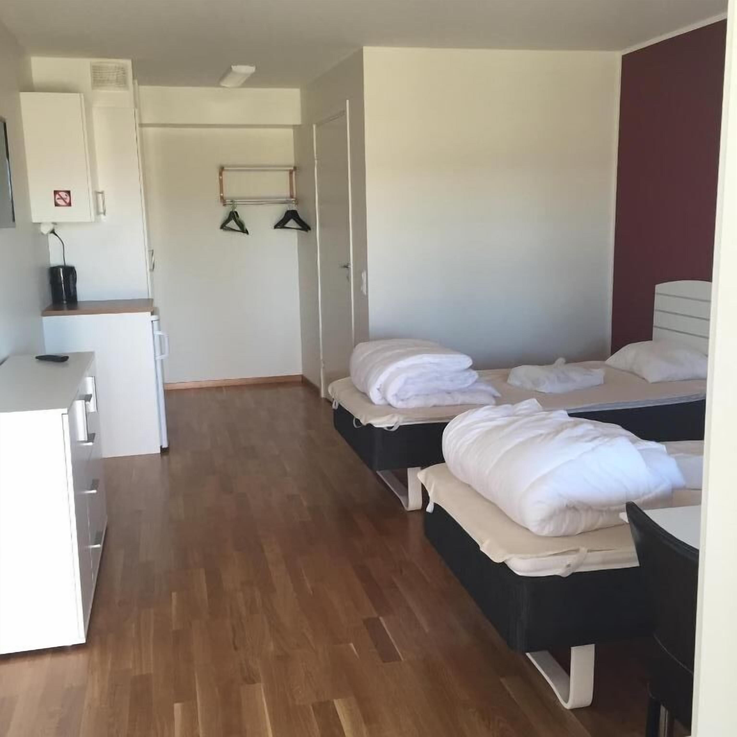 A hotel room with a wooden floor, a bed with white linens, a small desk with a computer, and a bathroom with a mirror and towel rack.
