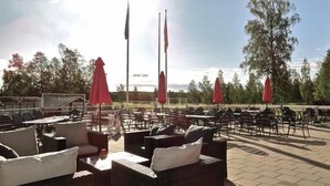 An outdoor seating area with tables and chairs, red umbrellas, and flags. - Piteå Golfhotell (Pitea)