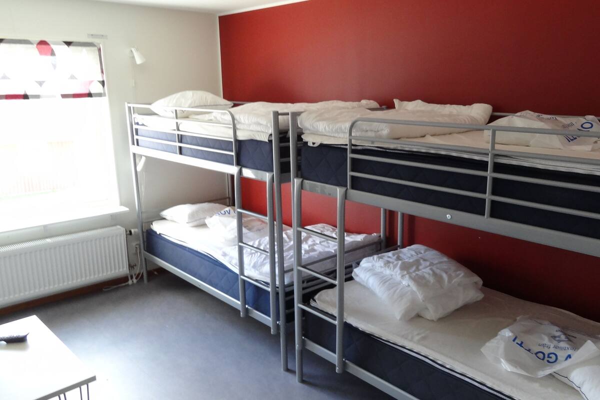 A bunk bed room with a red wall, white bedding, and a window with blinds.