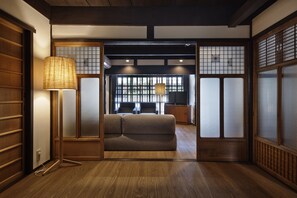 A traditional Japanese-style room with tatami flooring, a low wooden table, and a sliding door leading to a seating area with a sofa and chairs.