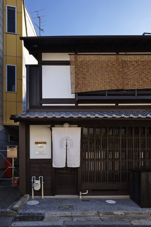 A traditional Japanese building with a wooden entrance, a tatami mat entrance, and a small outdoor seating area.