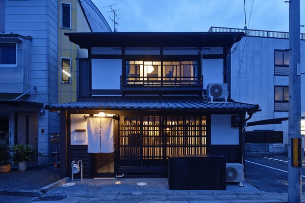 A traditional Japanese building with a wooden gate, a small porch, and a visible air conditioning unit.