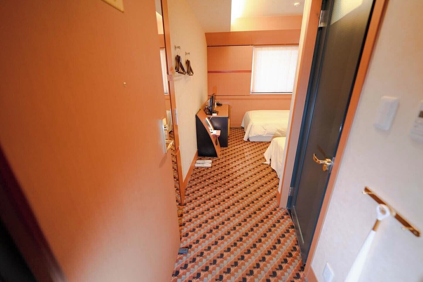 A hotel room with a patterned carpet, a bed, a desk, and a window with blinds.