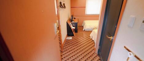 A hotel room with a patterned carpet, a bed, a desk, and a window with blinds.