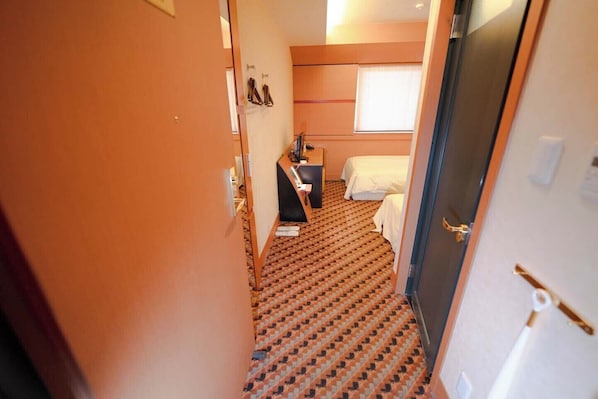 A hotel room with a patterned carpet, a bed, a desk, and a window with blinds.