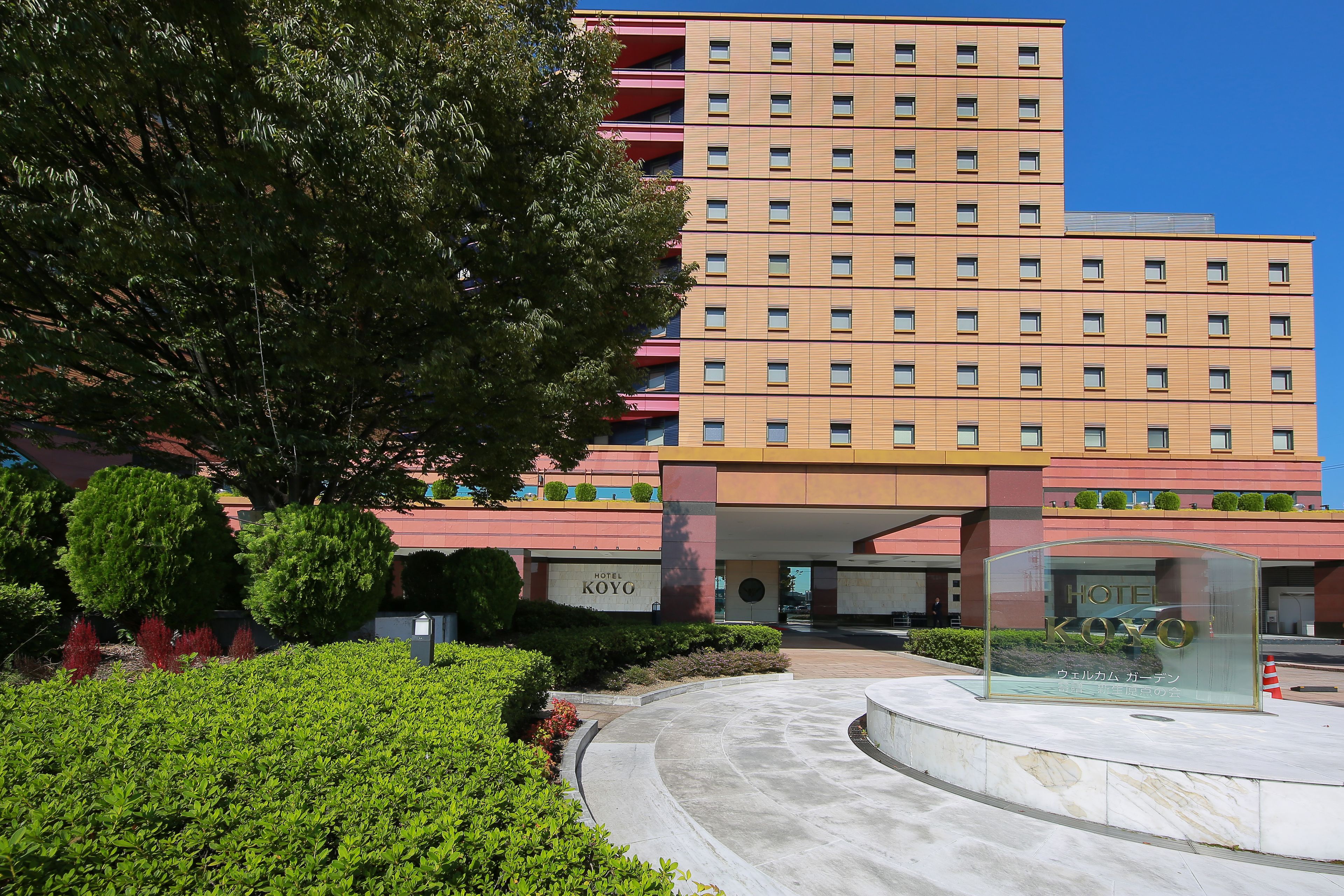 A hotel with a modern design, featuring a prominent entrance and a large tree in the foreground.