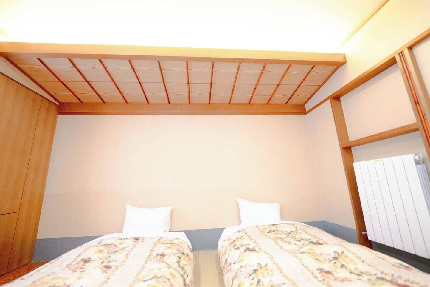Una habitación pequeña con dos camas, vigas de madera en el techo, un radiador y un armario.