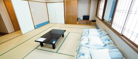 Une pièce avec un sol recouvert de tatamis, comprenant un futon servant de lit, une petite table basse et un téléviseur.