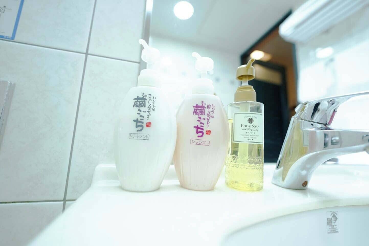 A bathroom with a sink, three bottles of toiletries, and a showerhead.