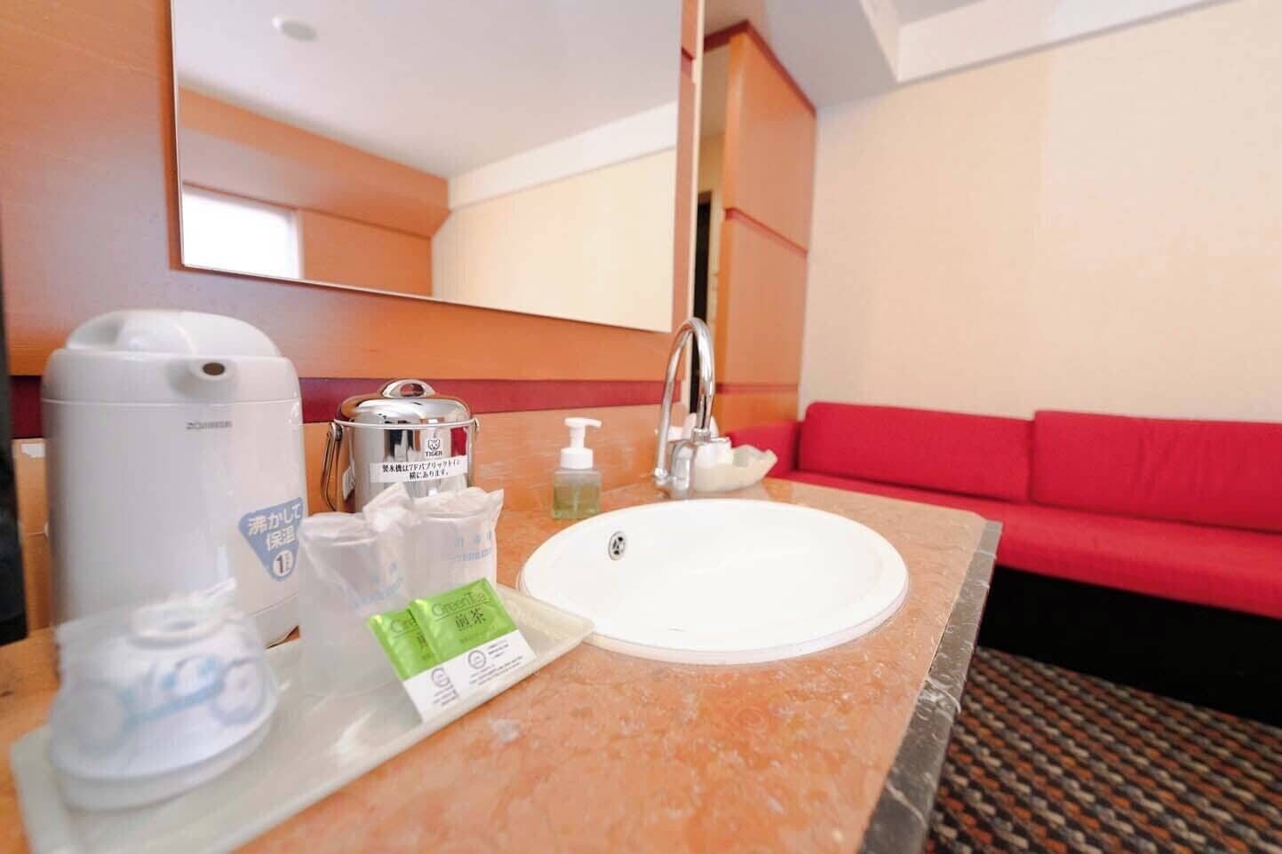 Une salle de bain d’hôtel avec un lavabo, un miroir, un canapé rouge et des articles de toilette.