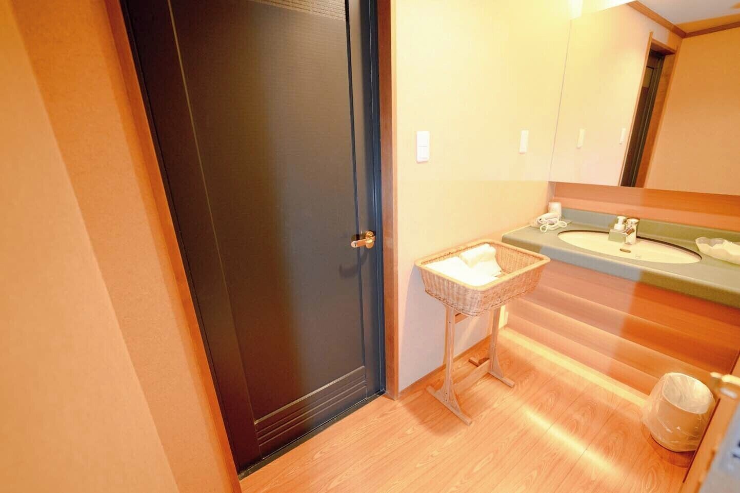 A bathroom with a dark door, a small sink, a wicker basket, and a mirror above the sink.