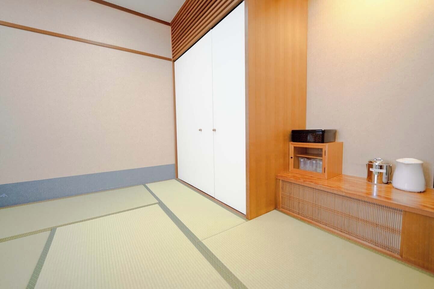 A traditional Japanese room with tatami flooring, a sliding door, a wooden cabinet with a microwave, and a small table with a kettle.