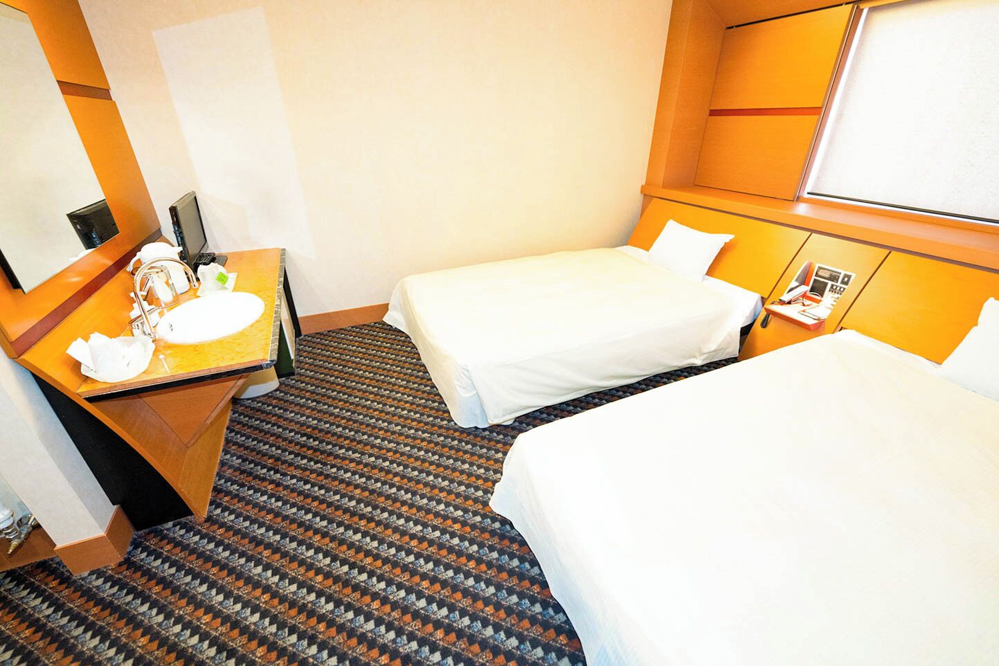 A hotel room with a bed, a desk with a sink, and a mirror.