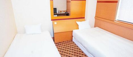 A hotel room with two single beds, a small table, a mirror, and a patterned rug.
